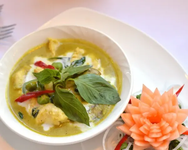 Zielone curry z kurczakiem, ozdobione bazylią i kwiatkiem z marchewki.