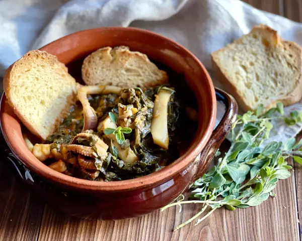 Seppie in zimino, un piatto tradizionale con seppie tenere e verdure, servito in una ciotola di terracotta con pane tostato e erbe aromatiche.