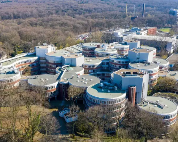 Luftaufnahme des Campus der **Uni Duisburg Essen** mit seinen charakteristischen runden Gebäuden, umgeben von Bäumen.