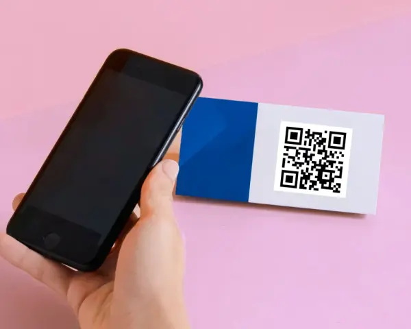 En hand håller en iPhone 6 för att scanna en QR-kod på ett kort med blått och vitt.