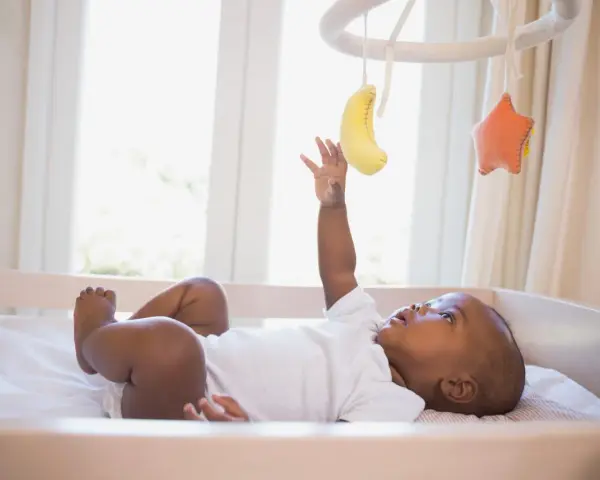 Maluch wyciąga rączkę do bananka i gwiazdki wiszących na karuzeli do łóżeczka.