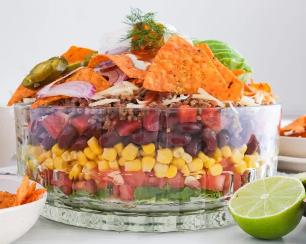 Schichtsalat mit Tortilla-Chips, Bohnen, Mais, Tomaten und Hackfleisch. Ein köstlicher, vegetarischer Nacho Salat, garniert mit Jalapeños und Sauerrahm.