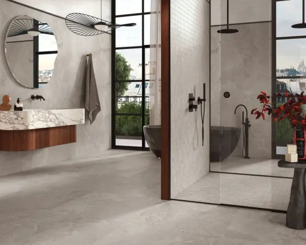 Salle de bain moderne avec baignoire îlot et douche vitrée. Le sol et les murs sont recouverts de carrelage gris, tandis que la paroi de douche est en petite faïence.