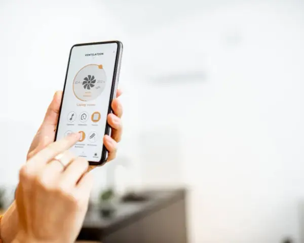 Mano usando un smartphone para encender calefacción a distancia en la sala de estar.