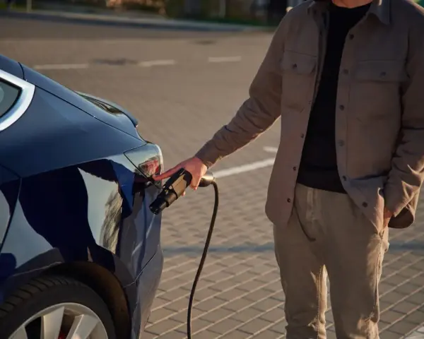 Mężczyzna podłącza ładowarkę do ciemnoniebieskiego samochodu elektrycznego. Zastanawiasz się, ile kosztuje ładowanie samochodu elektrycznego?
