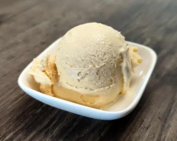 Cremiges Dulce de Leche Eis in einer weißen Schale auf Holzhintergrund.