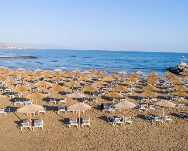Plaża sol marina beach crete z rzędami leżaków i parasoli, gotowa na gości. Błękitne morze i niebo tworzą idealne tło.