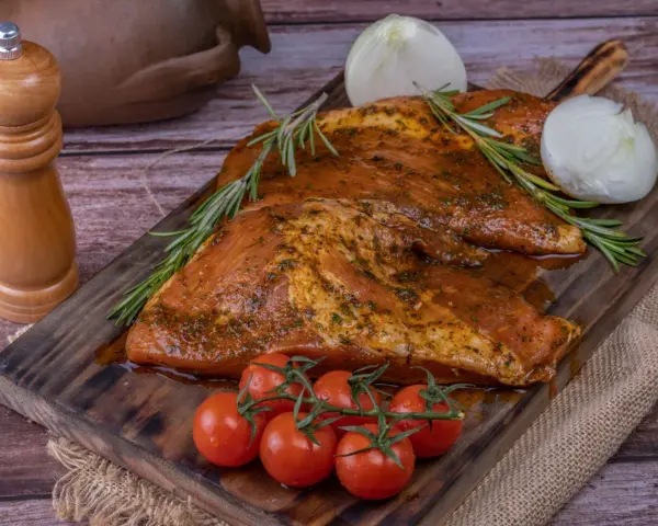 Carne marinada, lista para cocinar. El secreto ibérico se revela con romero, tomates y cebolla.