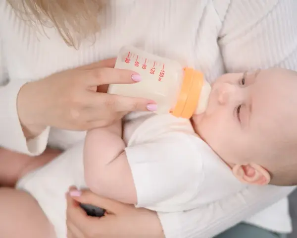 Mama karmi dziecko mlekiem modyfikowanym z butelki. Dziecko pije spokojnie, a mama czule go trzyma.
