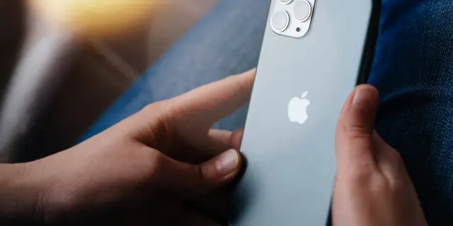 Dłonie trzymające szare iPhone'a z widocznym logo Apple i modułem aparatów.