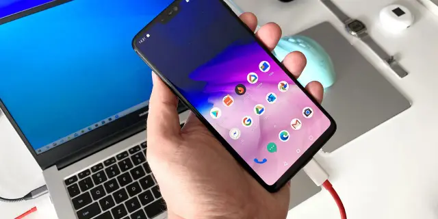 Dłoń trzyma smartfon podłączony kablem do laptopa.