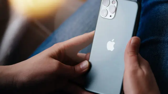 Dłonie trzymające szare iPhone'a z widocznym logo Apple i modułem aparatów.