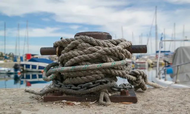 Grosse amarre enroulée sur une bitte d'amarrage, prête à supporter le poids d'un bateau. Le diamètre de la corde suggère une grande résistance.