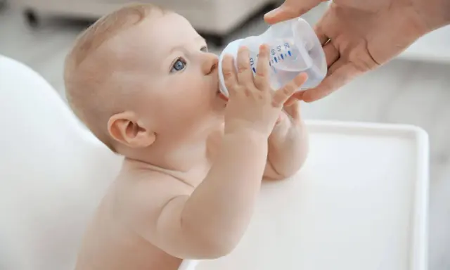 Niemowlę pije wodę z butelki. Od kiedy dziecko może pić wodę mineralną nieprzegotowaną? Od 6. miesiąca życia, gdy zaczyna rozszerzać dietę.