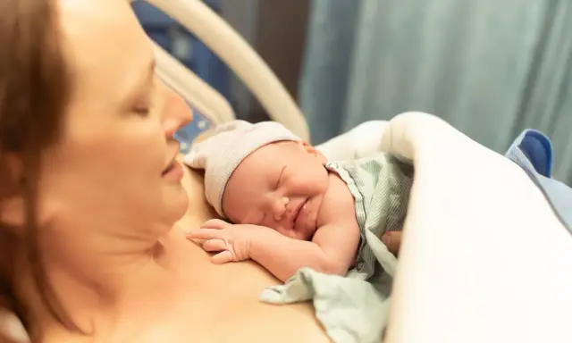 Noworodek śpi na piersi mamy, przygotowując się do karmienia. To piękny początek laktacji i więzi.