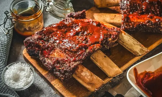 Saftige Rippchen mit BBQ-Sauce, perfekt für Ihre nächsten Grill Rezepte. Dazu grobes Salz und eine Schüssel Sauce.