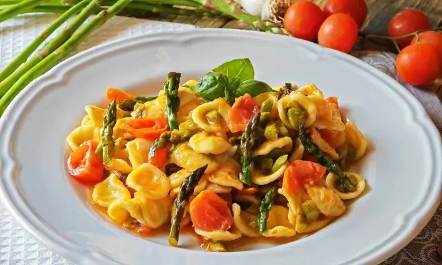 Piatto di orecchiette con asparagi freschi e pomodorini succosi, guarnito con basilico. Un classico della cucina italiana.