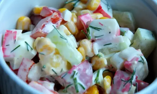 Pyszna sałatka z surimi, kukurydzy, ogórka i jajka, polana kremowym sosem z koperkiem.