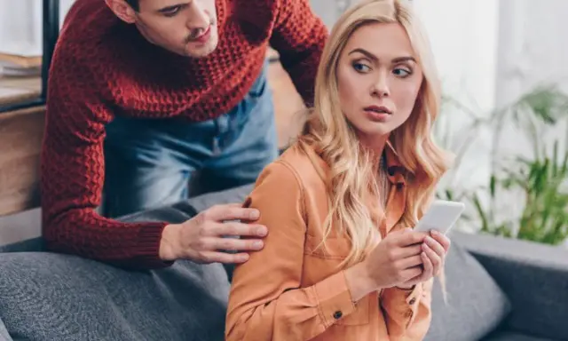 Chorobliwa zazdrość mężczyzny. Patrzy na telefon partnerki, która wygląda na zaniepokojoną.