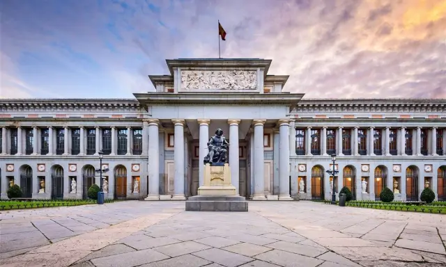 Das Prado Museum in Madrid, ein Meisterwerk der Architektur, mit einer Statue davor und einem dramatischen Himmel.