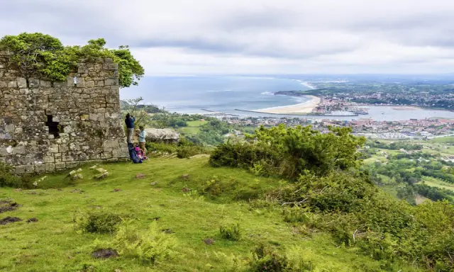 Zwei Wanderer genießen die Aussicht auf die Küstenstadt Irun, Spanien, von einer alten Ruine aus.