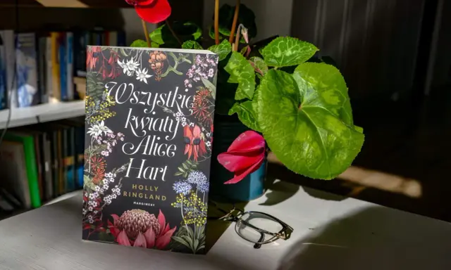 Okładka książki "Wszystkie kwiaty Alice Hart" z motywem roślinnym, obok cyklamen i okulary.