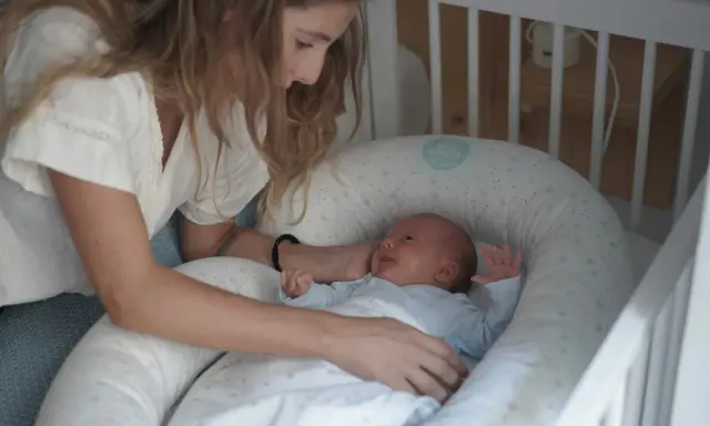 Madre observa a su bebé recién nacido, listo para sus siestas. El pequeño sonríe en su nido acogedor.