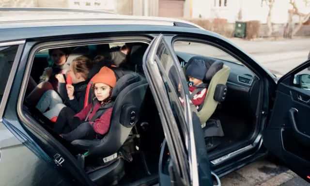Niños en asientos de coche, uno con gorro naranja. Guía visual para como colocar silla grupo 2 3 sin isofix.
