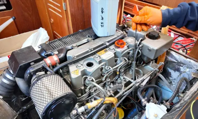 Main d'une personne en gant orange vérifiant le niveau d'huile d'un moteur 4 temps ne démarre pas. Bidon d'huile 25W40 à proximité.