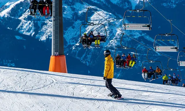 Snowboarder na stoku pod kolejką linową z narciarzami.