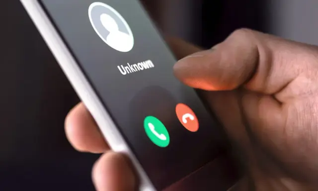Dłoń trzyma smartfon z ekranem połączenia przychodzącego od nieznanego numeru. Dowiedz się, jak dzwonić z zagranicy do Polski na komórkę.