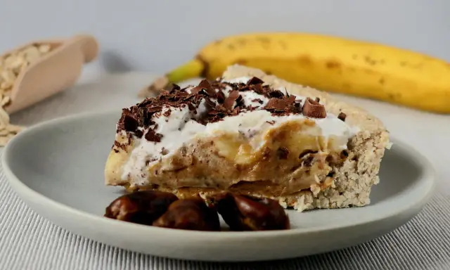 Pyszny sernik banoffee z bananami, karmelem i bitą śmietaną, posypany czekoladą. Obok leży dojrzały banan.