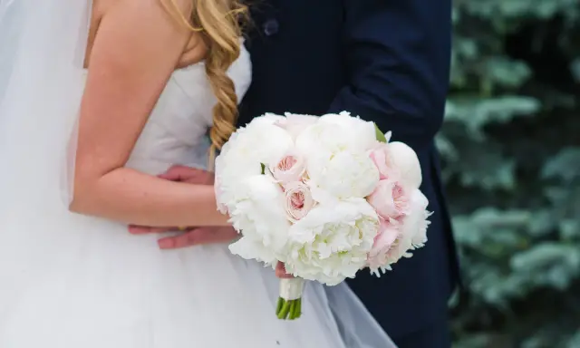 Piękny bukiet ślubny piwonie i eustoma w dłoniach pary młodej. Delikatne białe i różowe kwiaty tworzą romantyczną kompozycję.