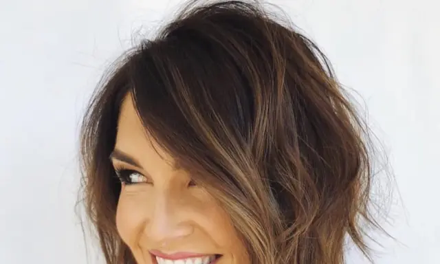 Uśmiechnięta kobieta z brązowymi włosami, prezentująca modny **bob asymetryczny cieniowany** z subtelnymi refleksami.