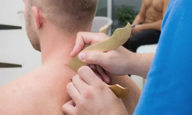 Masaż karku z użyciem narzędzi do pinoterapii. Terapeuta wykonuje zabieg na skórze pacjenta.