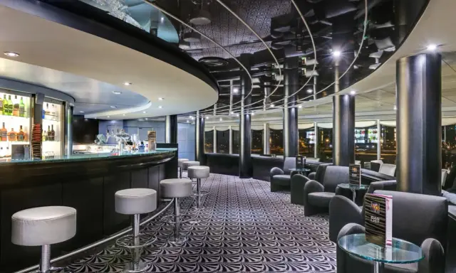 A modern bar with a curved counter, stools, lounge seating, and a patterned carpet.