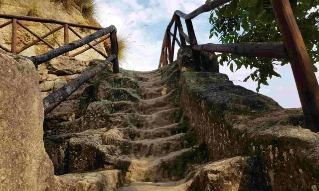 Antica scala in pietra scavata nella roccia, con ringhiera in legno, che conduce verso l'alto, evocando un'esplorazione in una grotta in Calabria.