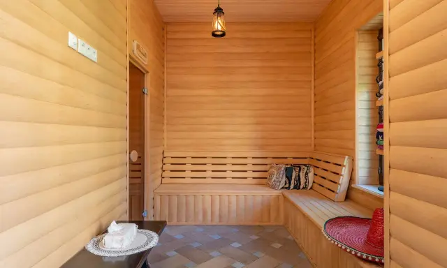 Interior de madera con bancos para relajarse, mostrando varios tipos de saunas. Un sombrero rojo y cojines decoran el espacio.