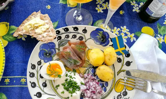 En härlig sillunch midsommar med färskpotatis, ägg, gräddfil och rödlök. En svensk flagga vajar glatt.