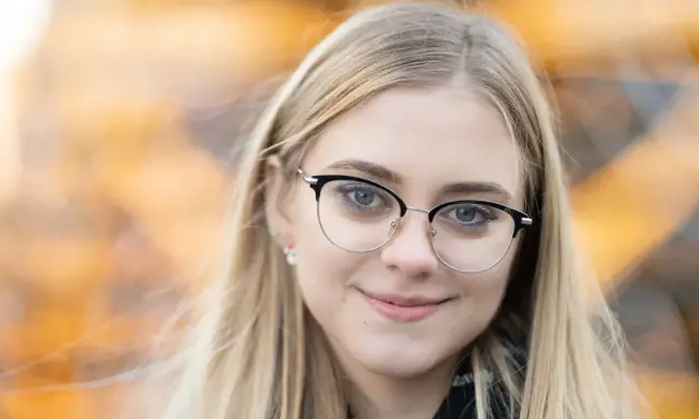 Uśmiechnięta blondynka w okularach, z rozmyciem tła. Idealna ogniskowa do portretu, podkreślająca oczy.