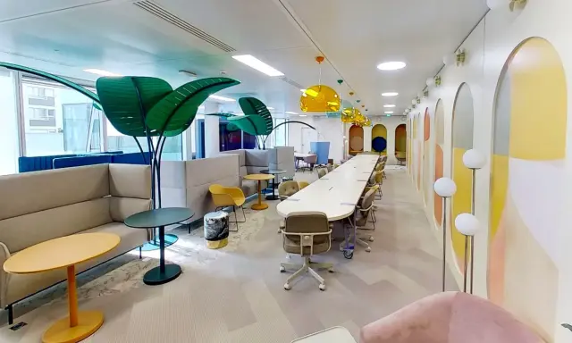 Espace de travail moderne et coloré, ce **flex office** offre des zones de réunion, des canapés confortables et des plantes décoratives pour un environnement stimulant.