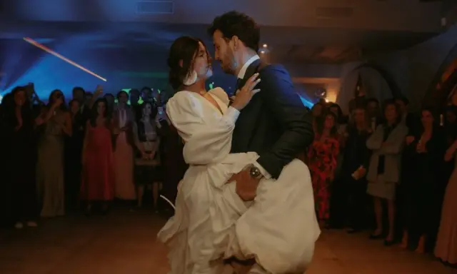 Novios bailando su vals boda, rodeados de invitados expectantes. La novia, con un vestido blanco voluminoso, es alzada por el novio.