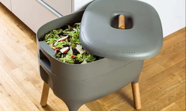 Compostador gris con restos de comida y hojas. Aprende como hacer compost para un jardín sostenible.