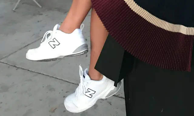White New Balance dad shoes with a black "N" logo, paired with a pleated skirt.