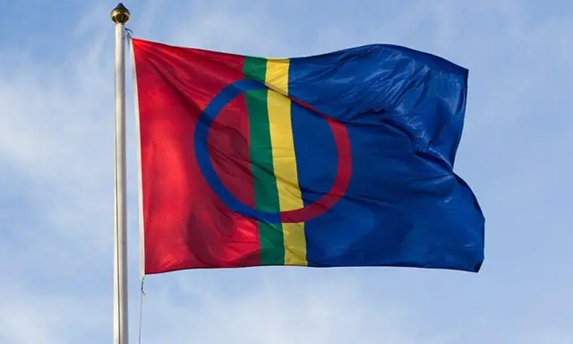 Samiska flaggan vajar stolt mot en blå himmel, en symbol för samiska nationaldagen och ett folk med djupa rötter.
