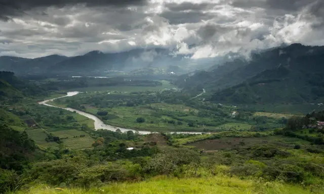 Ein gewundener Fluss schlängelt sich durch ein grünes Tal in Costa Rica. Wolken ziehen über die Berge, die das Bild umrahmen.