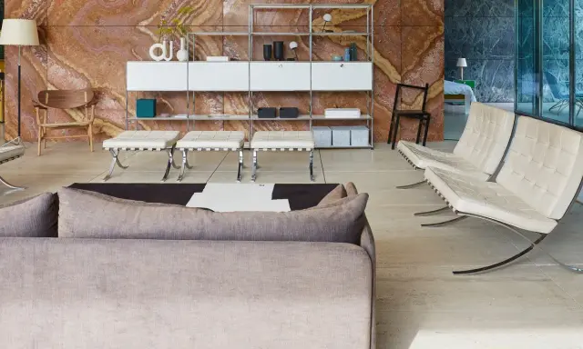 Soggiorno moderno con divano grigio, poltrone in pelle bianca e sgabelli, su sfondo di travertino rosso. Il **case design** è elegante e funzionale.