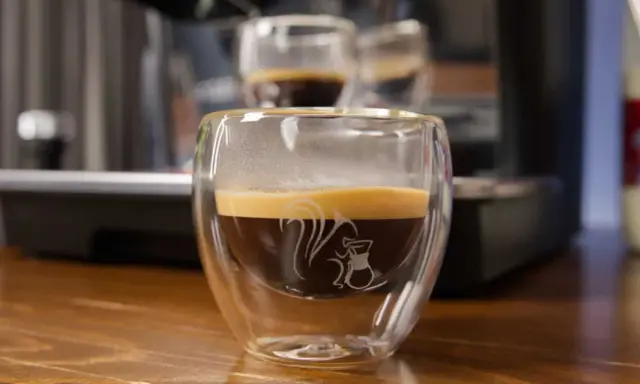 Ein dampfender doppio macchiato in einem doppelwandigen Glas mit einem Eichhörnchen-Motiv.