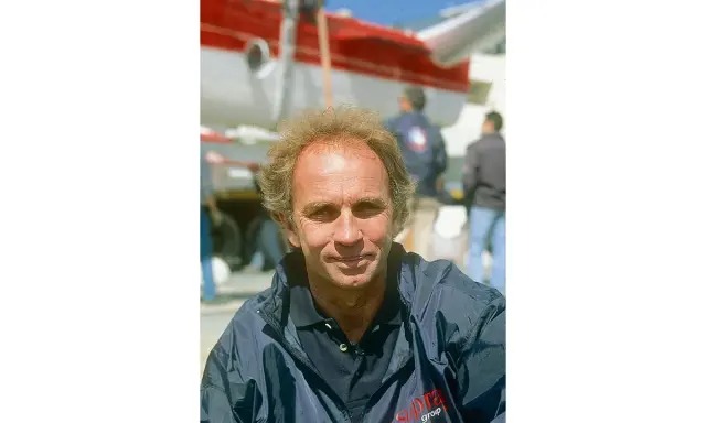 Jean-Claude Parisis, navigateur, souriant devant un avion rouge et blanc.