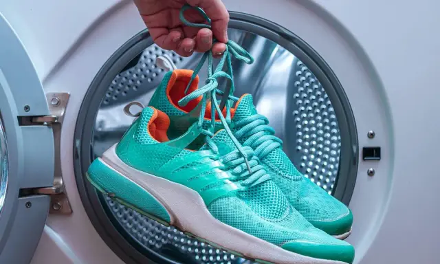 Türkisfarbene Laufschuhe werden vor dem Waschen in der Waschmaschine gehalten.